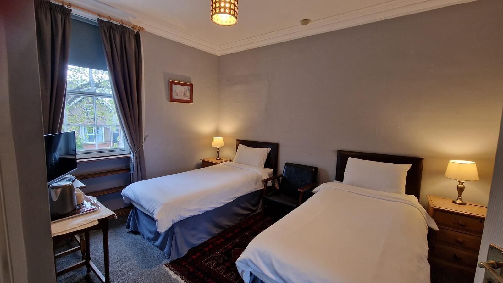 A hotel room with two beds, a TV, a desk with a lamp, and a window with curtains.