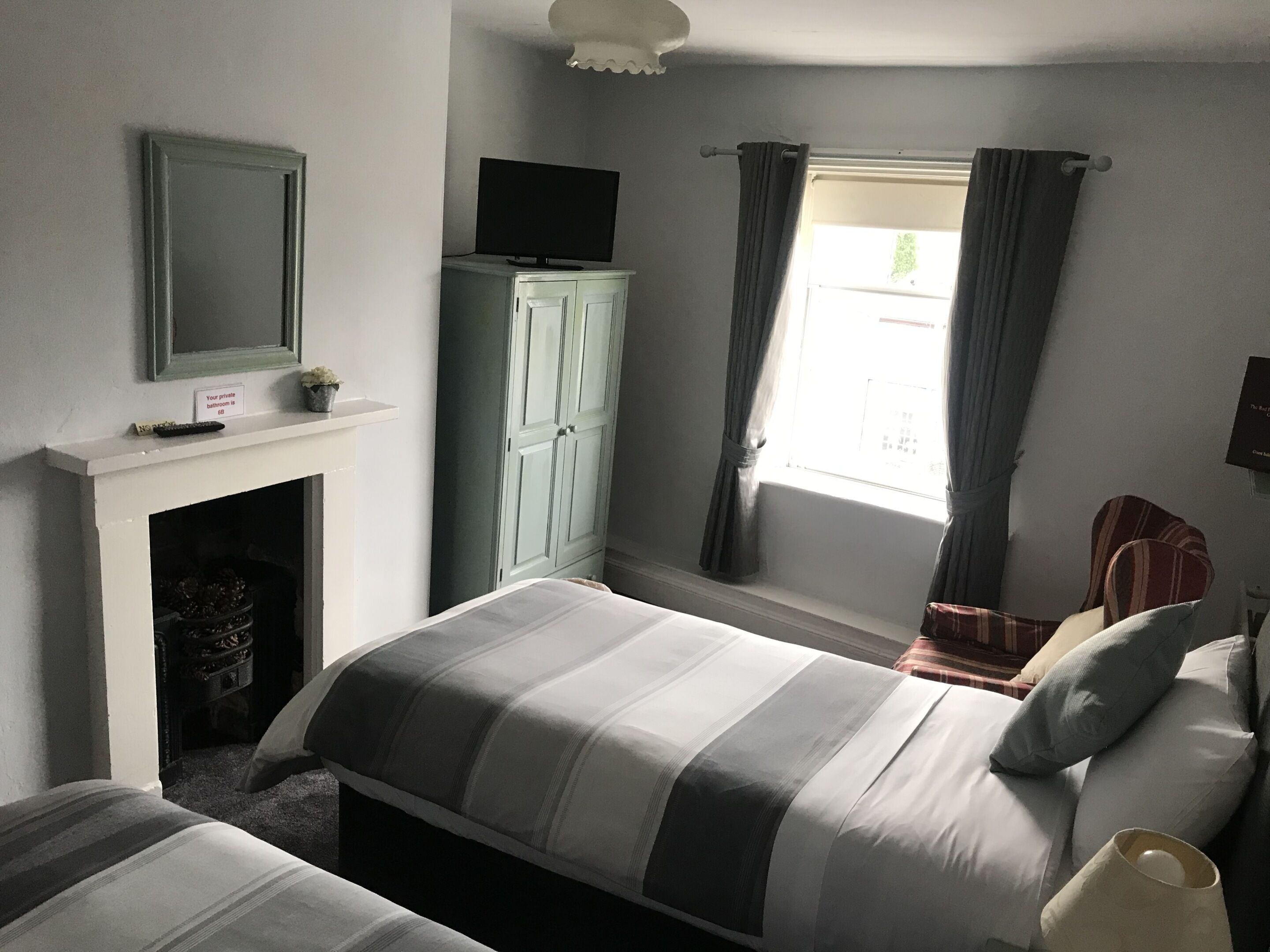 A bedroom with a bed, a wardrobe, a television, a fireplace, and a window with curtains.