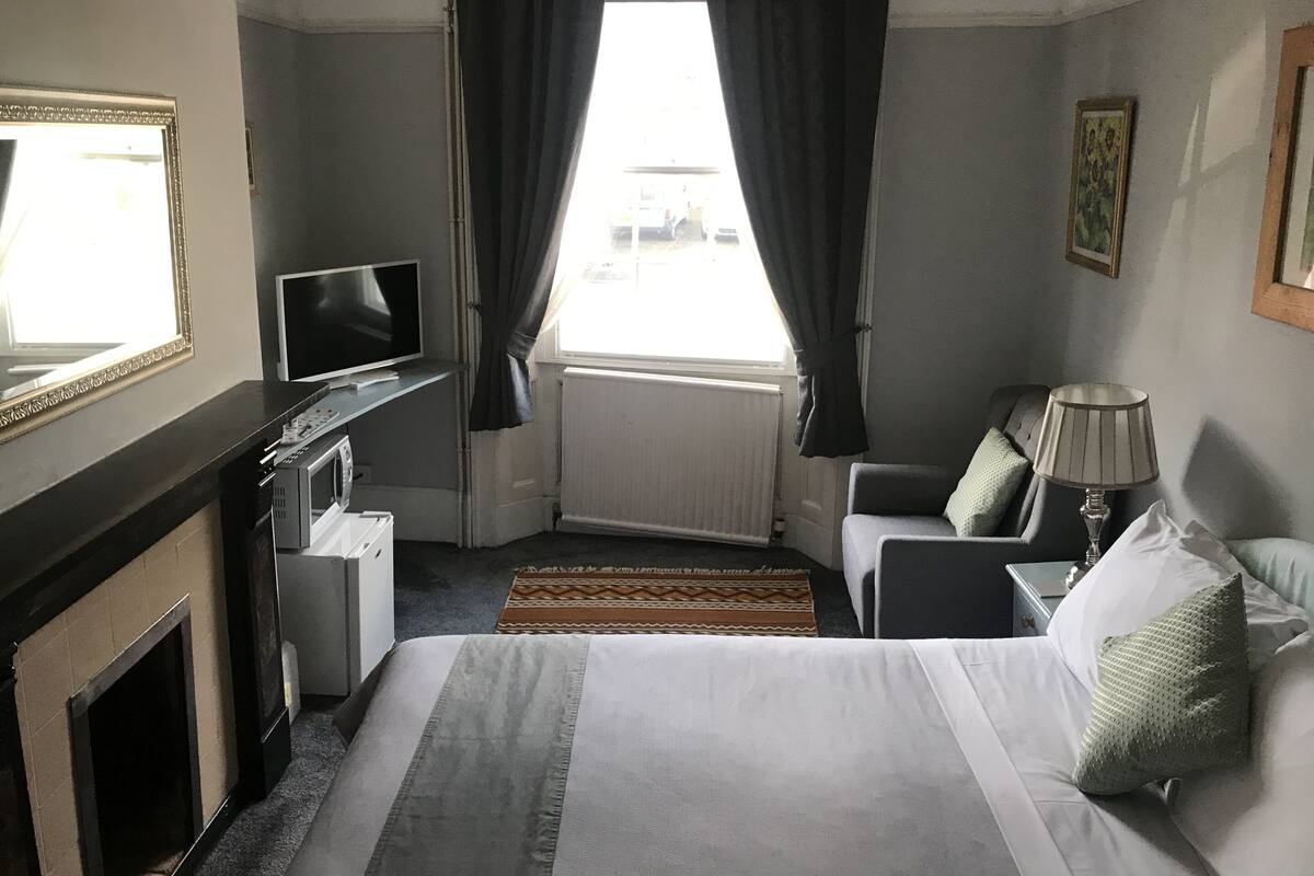 A hotel room with a bed, a desk with a computer, a television, a lamp, and a fireplace.
