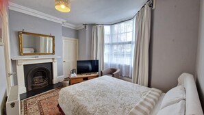 A hotel room with a bed, a television, a fireplace, and a window with curtains. - The Red House Guest House (Grantham)