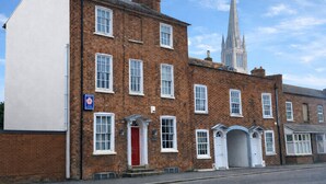 A traditional brick building with multiple windows and a red door, adjacent to a church with a tall spire. - The Red House Guest House (Grantham)