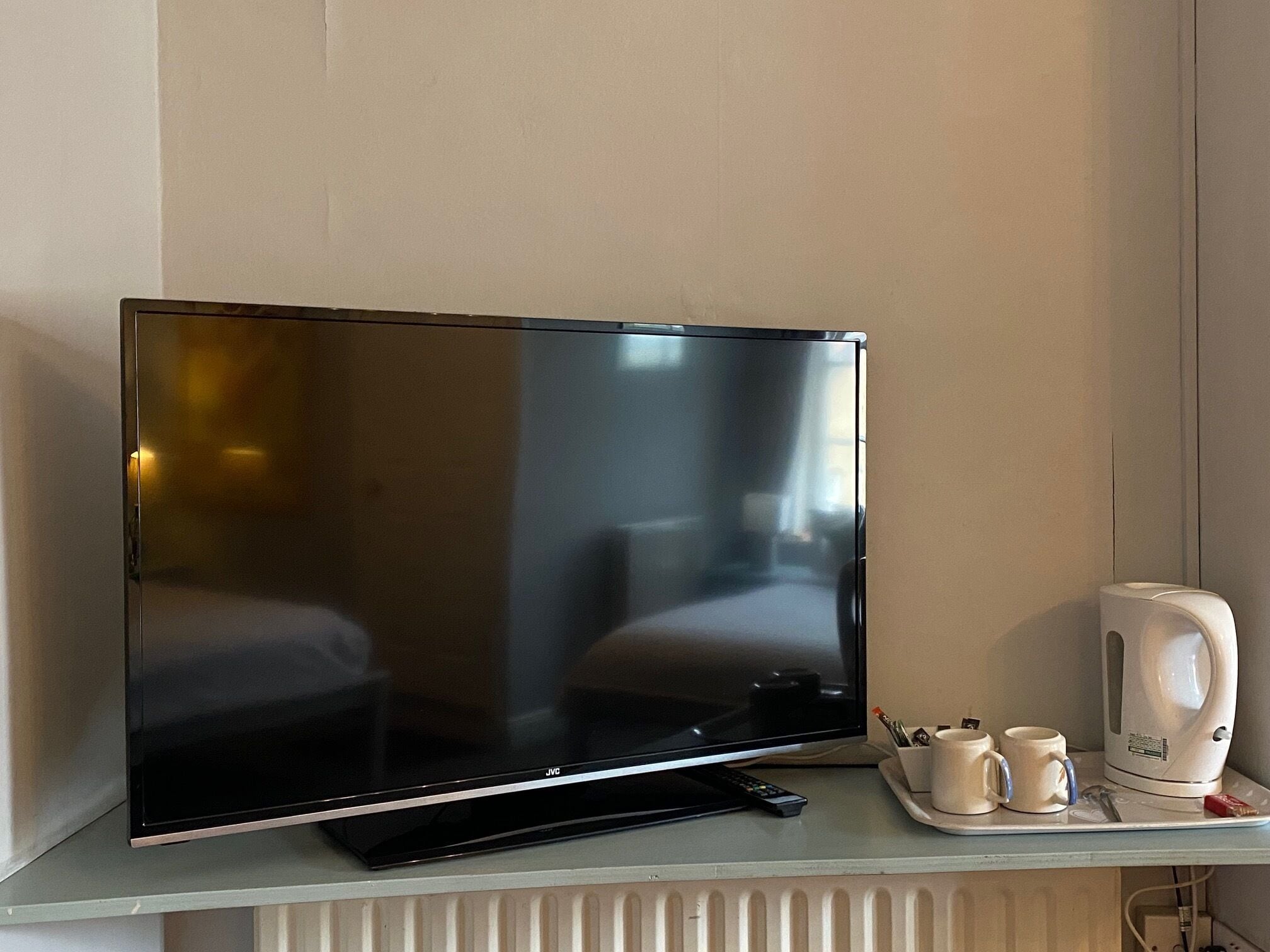 A flat-screen TV on a shelf, a remote control, two mugs, and a white electric kettle.