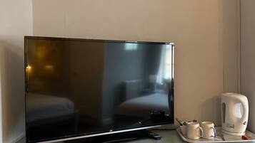 A flat-screen TV on a shelf, a remote control, two mugs, and a white electric kettle.
