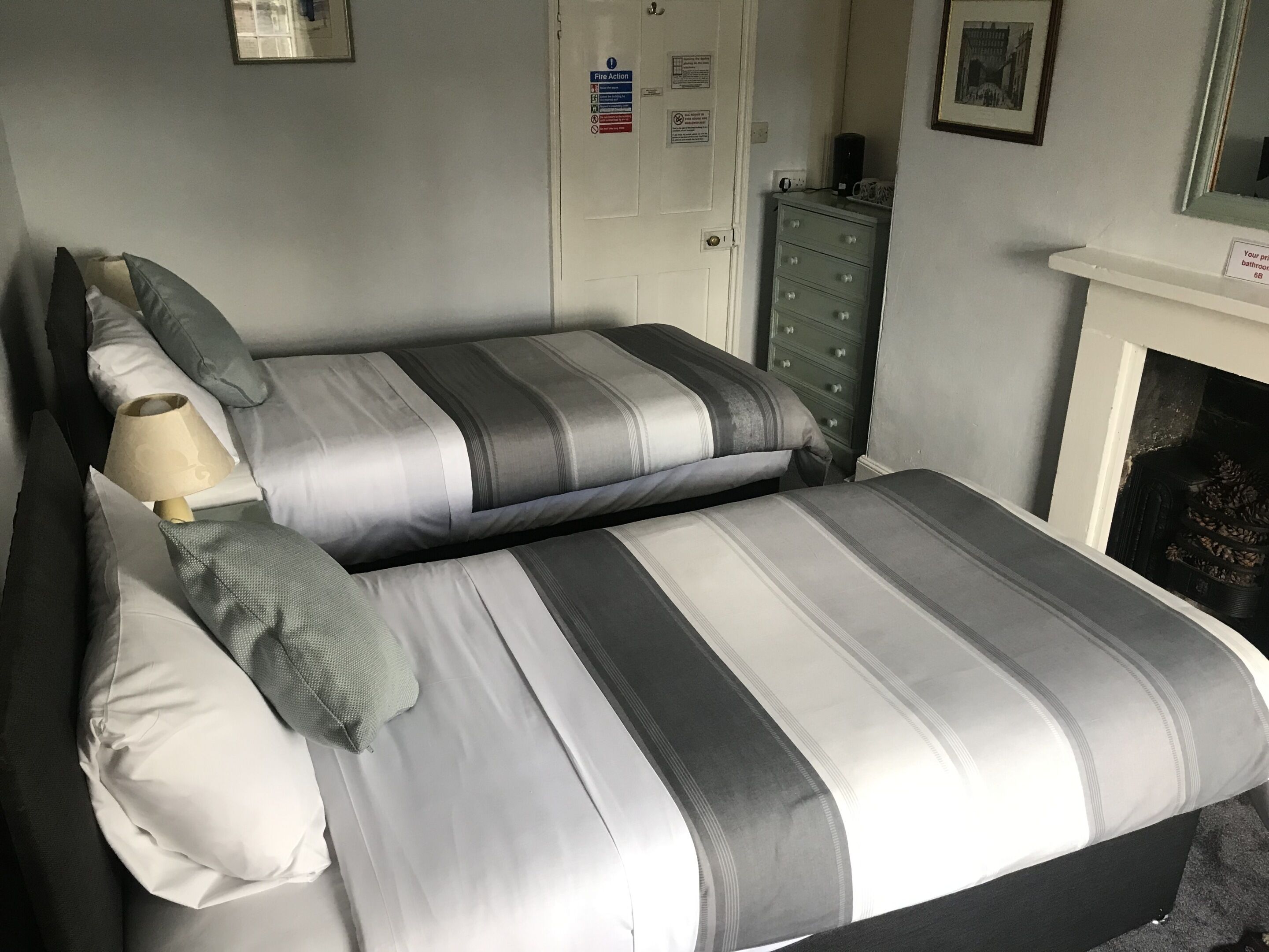 Un lit double avec une parure de lit à rayures grises et blanches, une lampe de chevet et une commode avec des tiroirs.