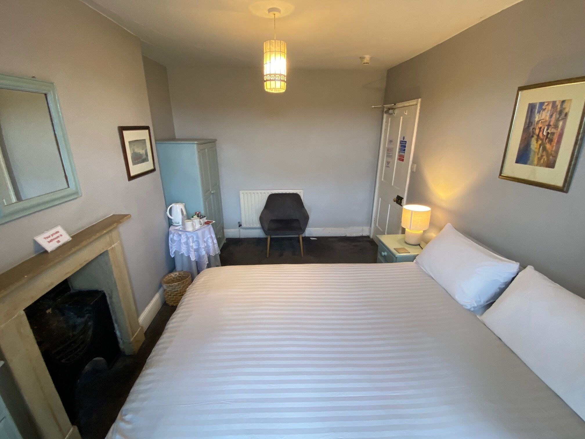 Hotellihuone, jossa on suuri sänky, tuoli, pieni pöytä lampun kanssa, takka ja patteri.