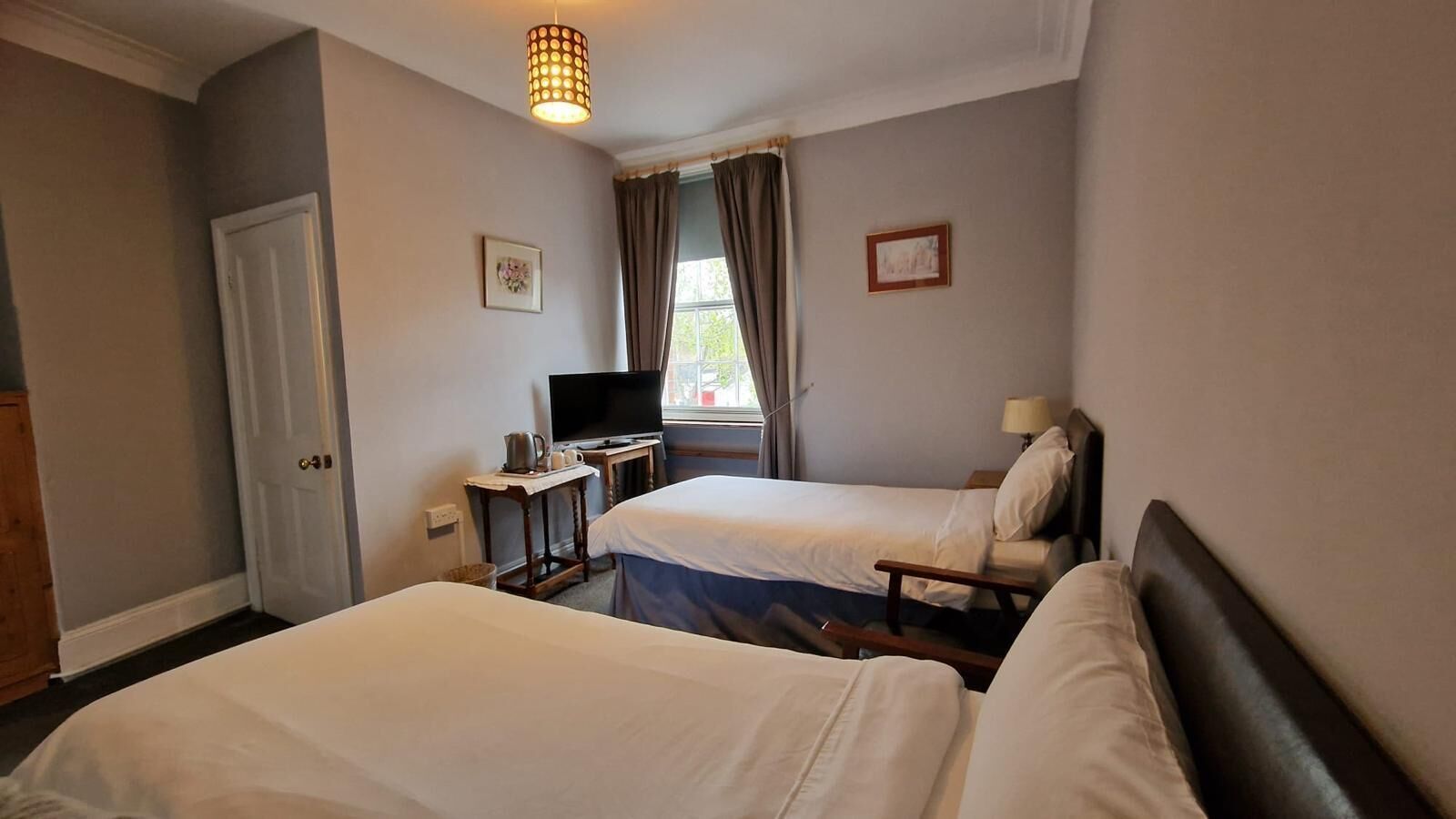 A hotel room with two beds, a television, a small table with a pitcher, and a window with curtains.