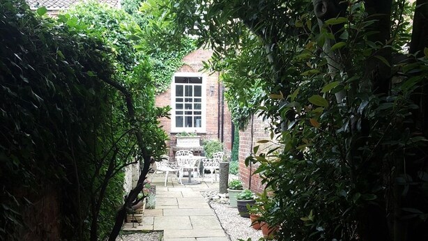 A narrow pathway leading to a brick building with a large window. - The Red House Guest House (Grantham)