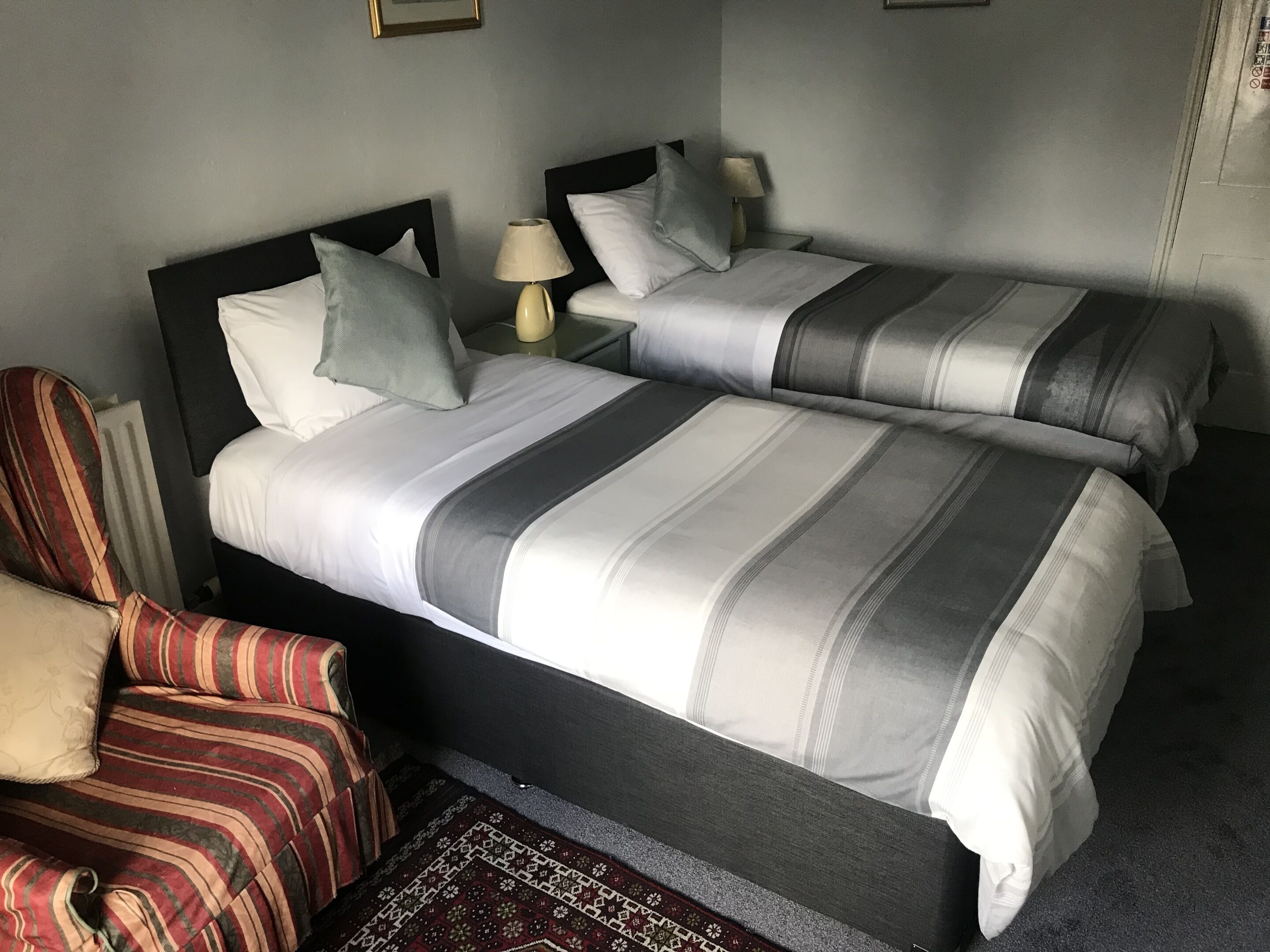 A hotel room with two beds, a chair, and a lamp.