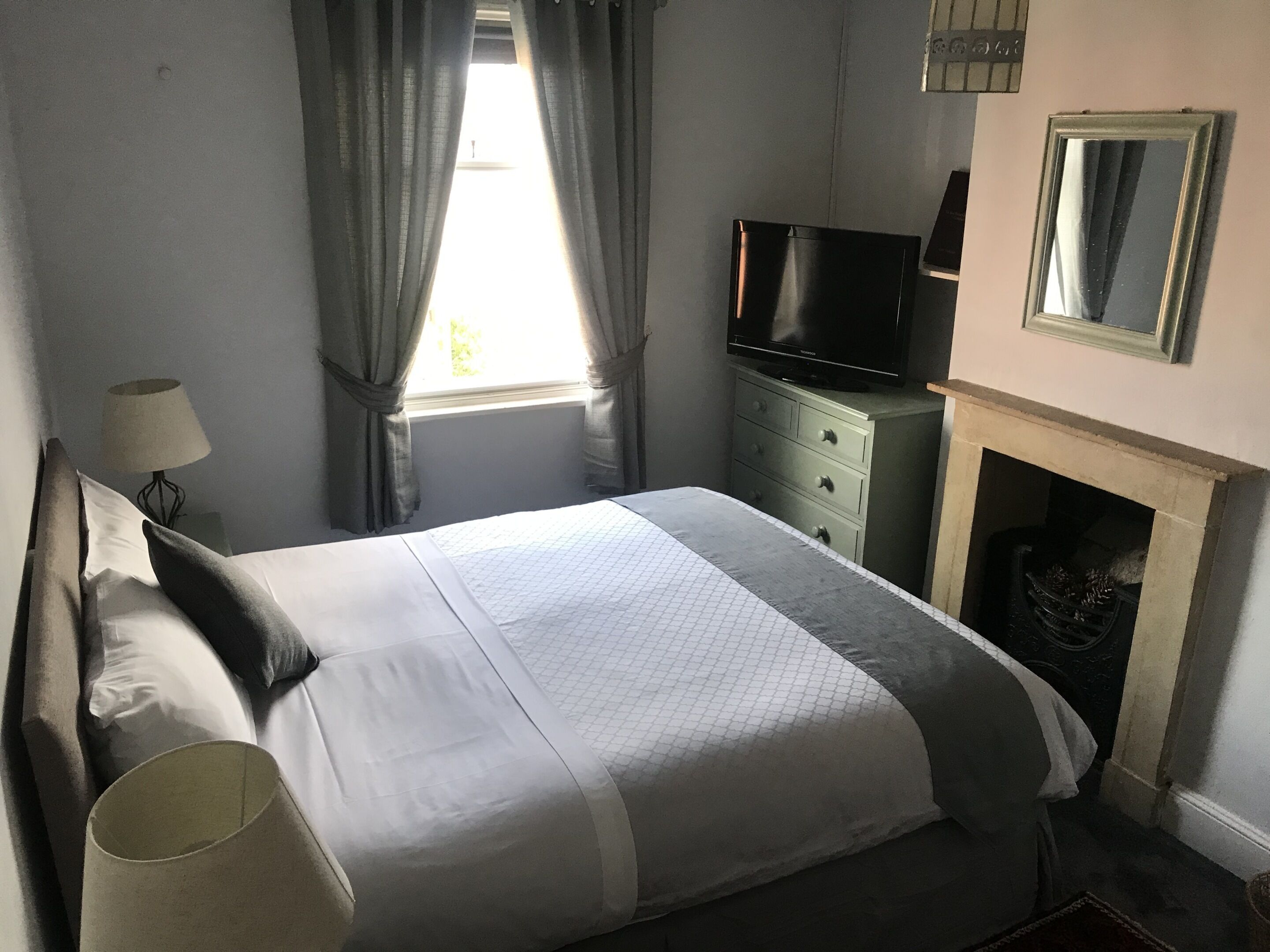 Ein ordentlich bezogenes Bett mit Kissen, ein Fernseher auf einer Kommode, eine Lampe und ein Kamin.