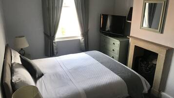 Ein ordentlich bezogenes Bett mit Kissen, ein Fernseher auf einer Kommode, eine Lampe und ein Kamin.