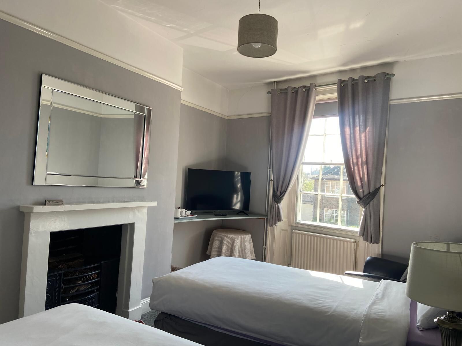 A hotel room with a fireplace, a television, two beds, a window with curtains, and a hanging light fixture.