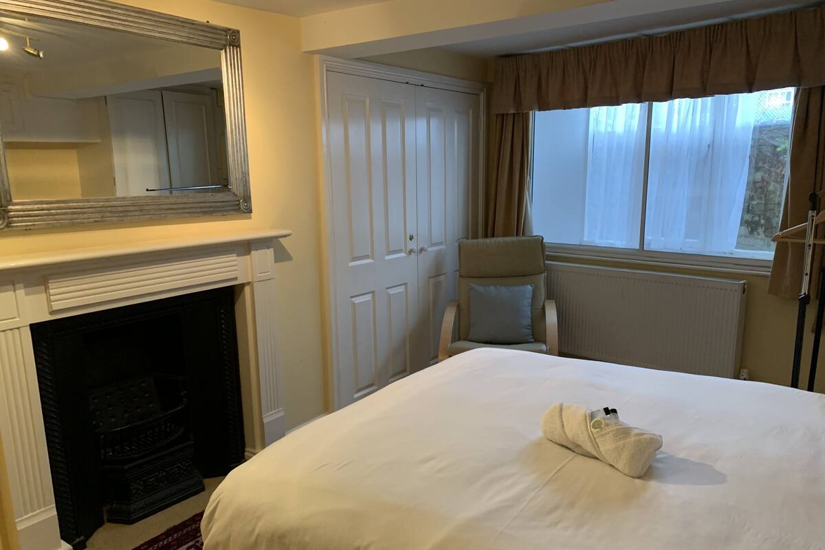A hotel room with a large bed, a fireplace, a wardrobe, and a window with curtains.