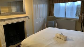 Une chambre d’hôtel avec un grand lit, une cheminée, une armoire et une fenêtre avec des rideaux.