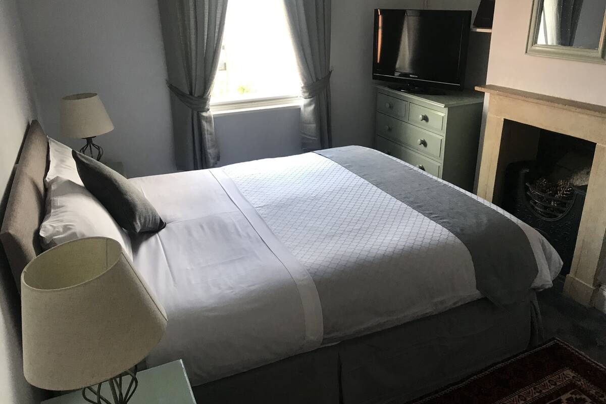 A neatly made bed with a white and gray bedspread, a bedside lamp, and a television on a dresser.