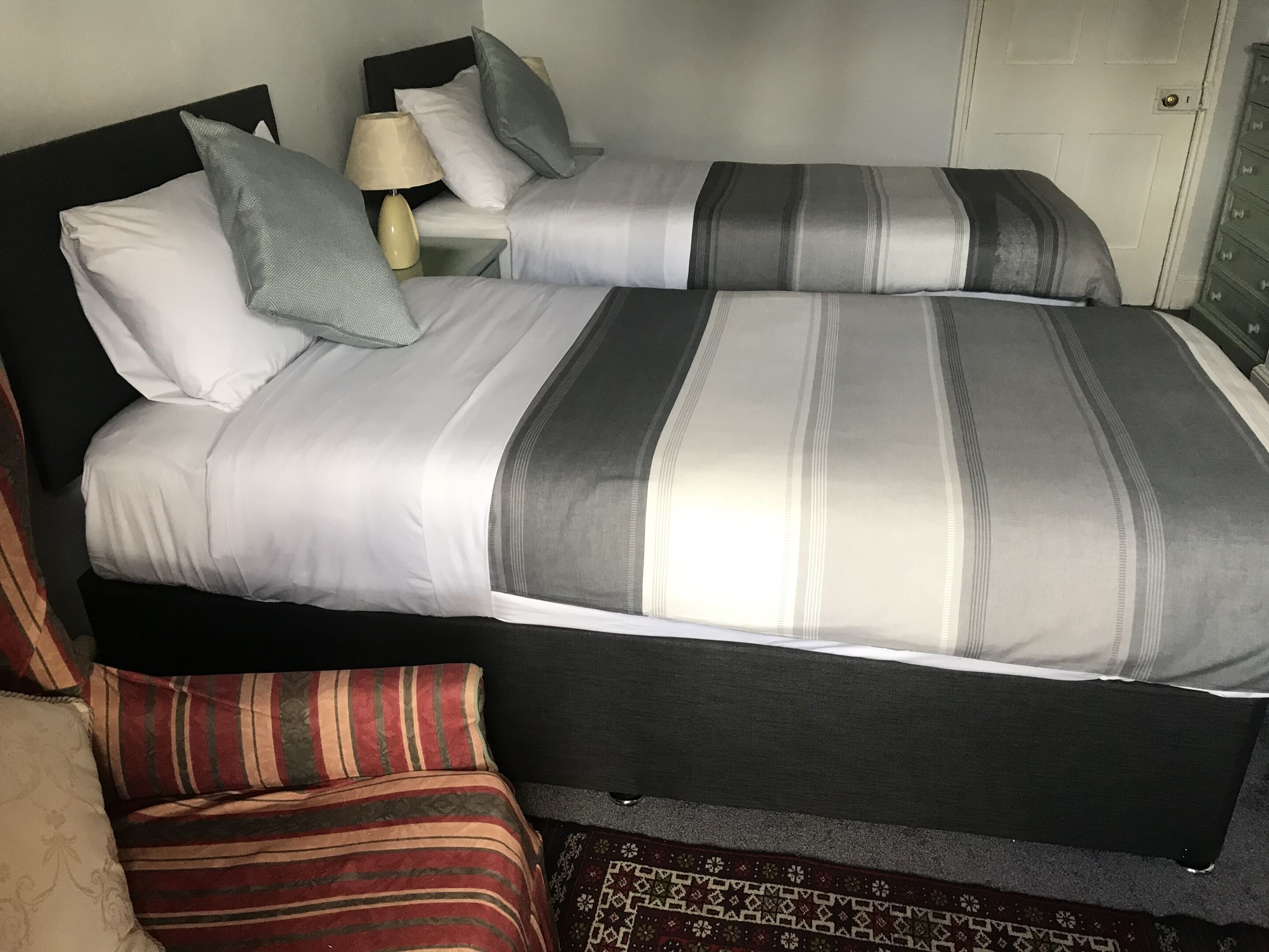 Una cama bien hecha con ropa de cama a rayas y almohadas, una lámpara de noche y una mesita de noche pequeña.