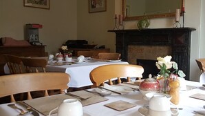 A dining room with a table set for four, a fireplace, and framed artwork on the walls. - The Red House Guest House (Grantham)