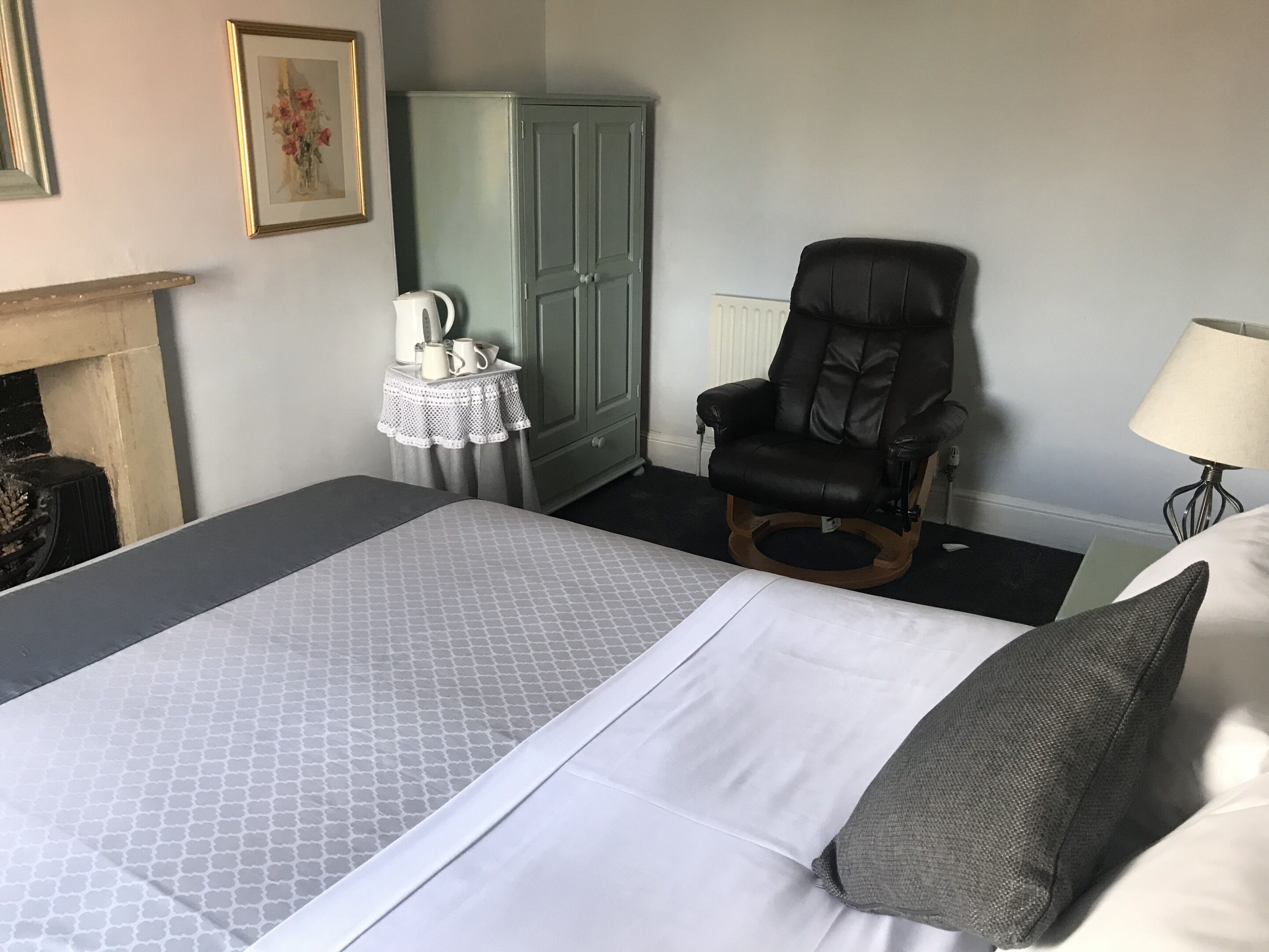 A neatly arranged bedroom with a bed, a chair, a cabinet, and a lamp.