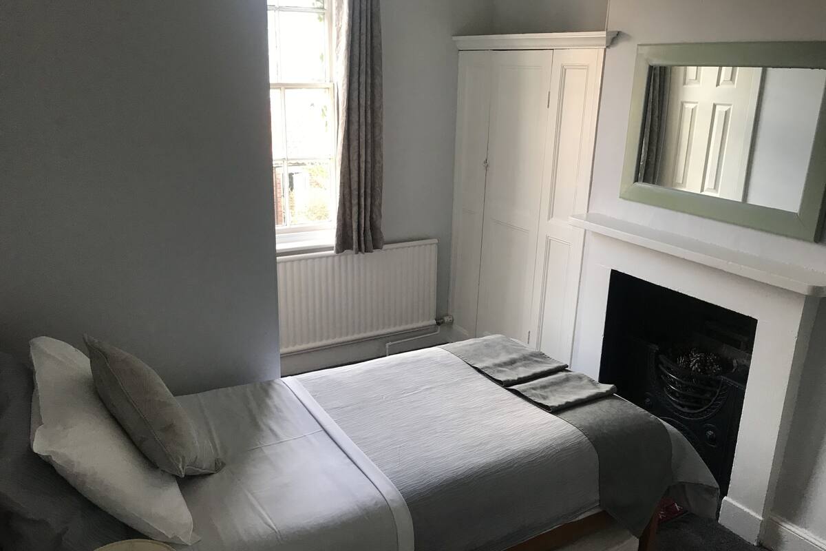 A bedroom with a bed, a wardrobe, a fireplace, and a window.
