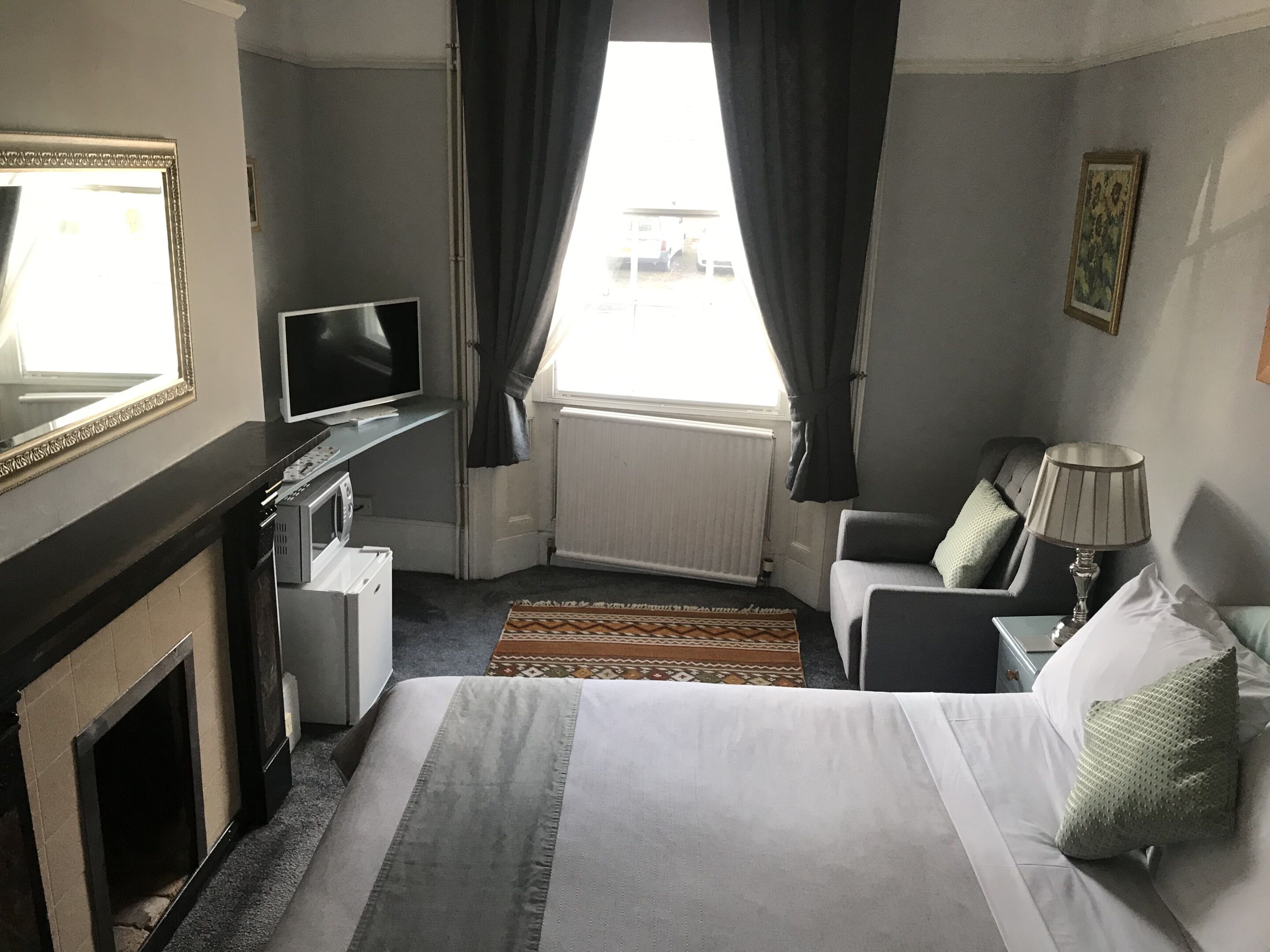 Habitación de hotel con cama, escritorio con televisor, lámpara, chimenea y ventana con cortinas.