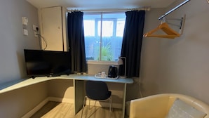 A small room with a desk, a chair, a TV, a window with curtains, a sofa, and a hanging coat rack. - The Red House Guest House (Grantham)