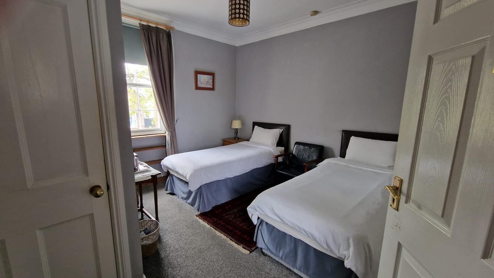 A hotel room with two beds, a desk, a chair, a window with curtains, and a picture on the wall.