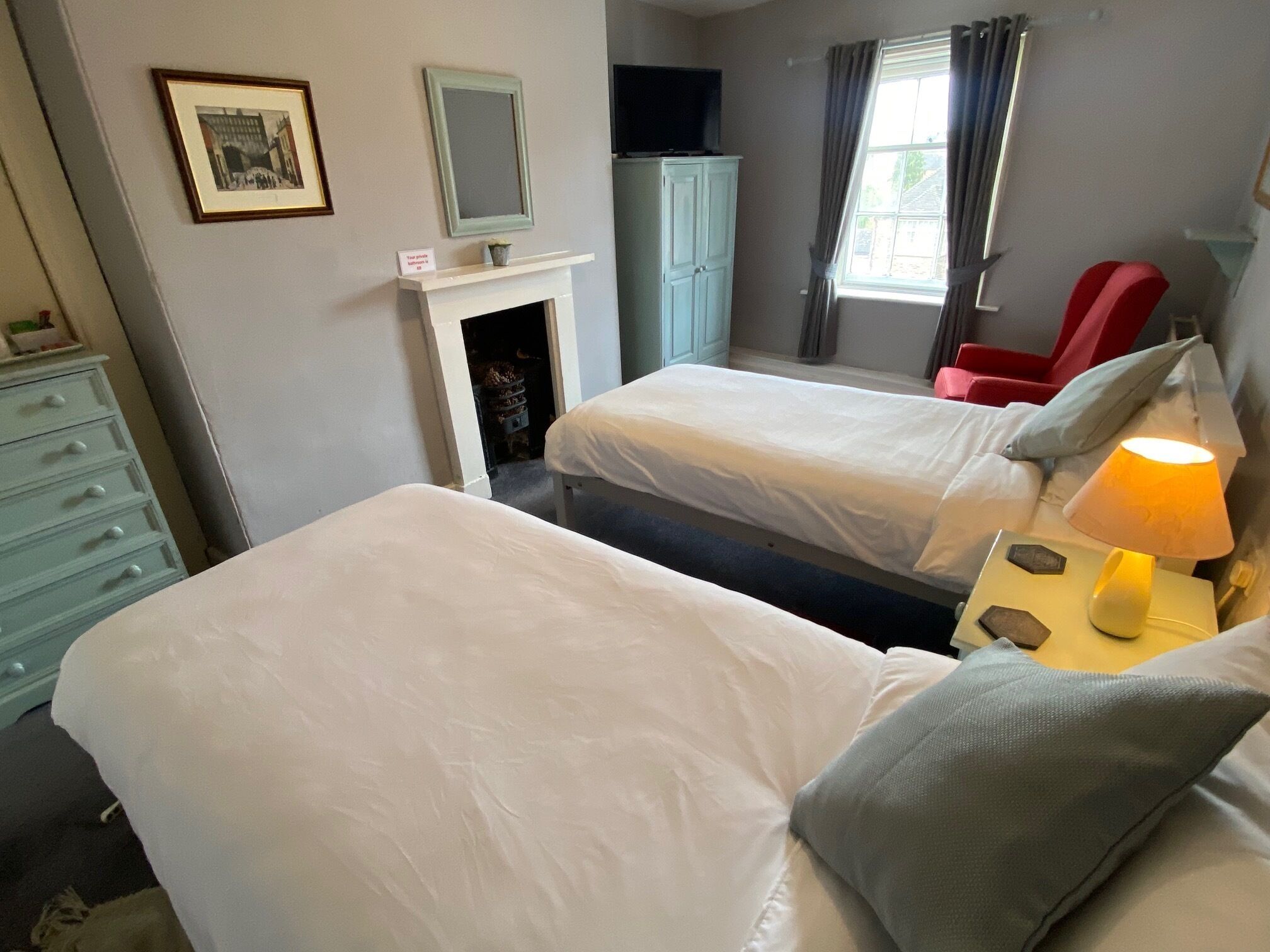 A room with two beds, a dresser, a television, and a fireplace.