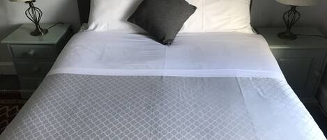 A neatly made bed with a patterned bedspread, two pillows, and two bedside lamps on matching nightstands.