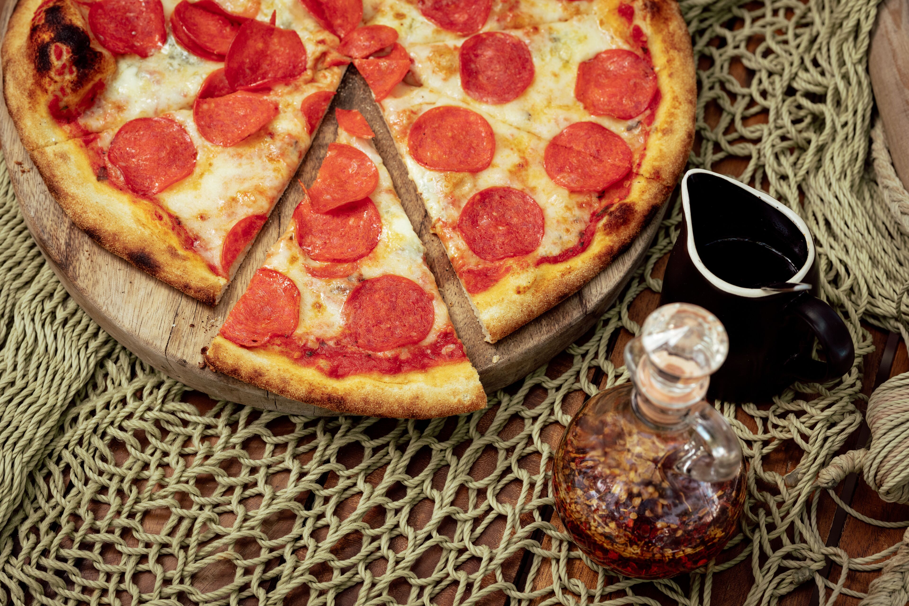 A pizza with pepperoni slices on a wooden board, accompanied by a bottle and a small pitcher.