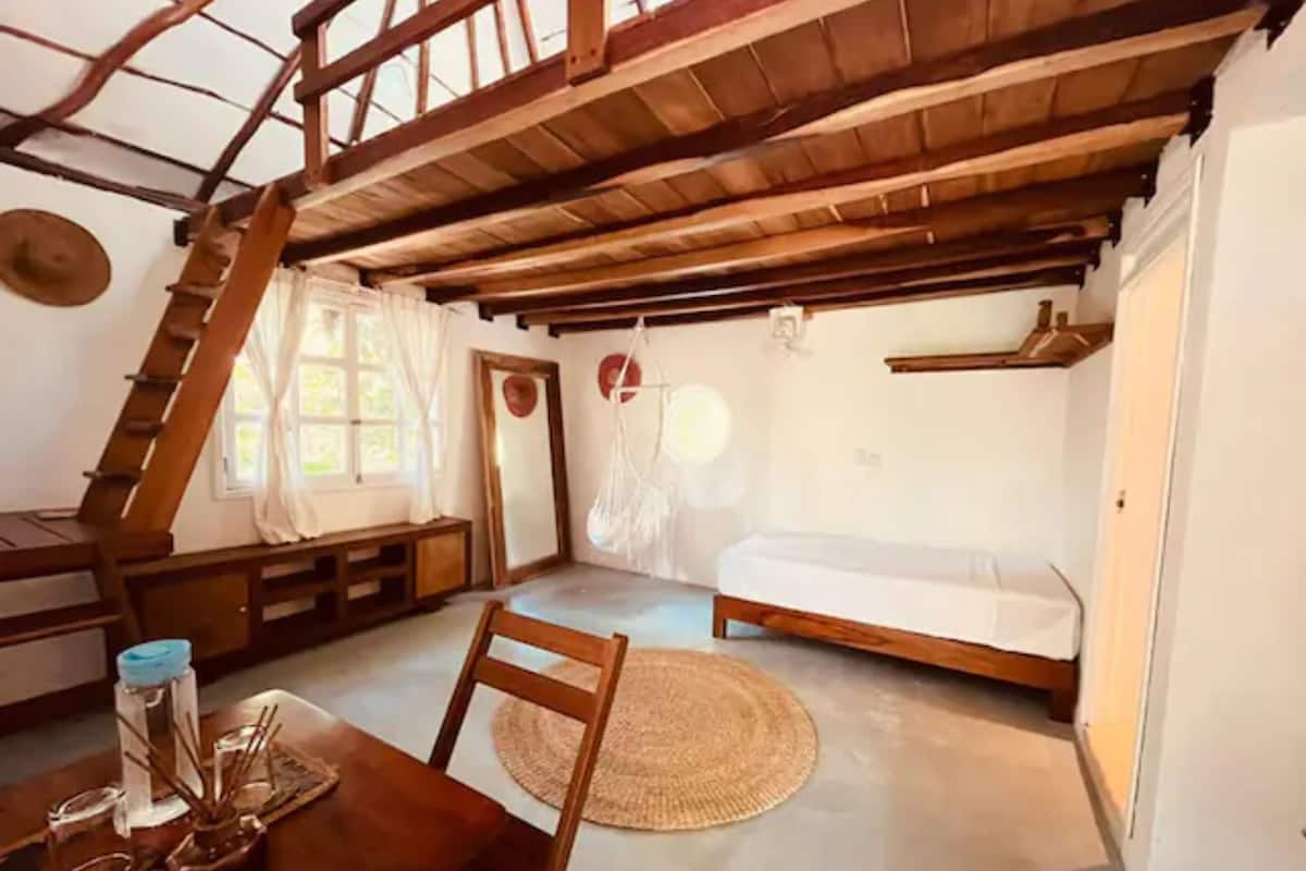 A rustic room with a loft bed, a wooden desk, and a dining table.