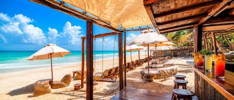 A beachside bar with wooden deck, lounge chairs, and umbrellas.