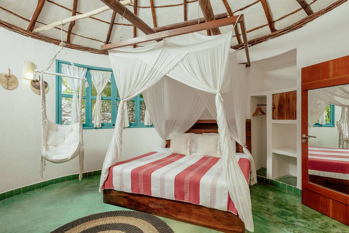 A room with a bed, a hanging chair, and a window with curtains.