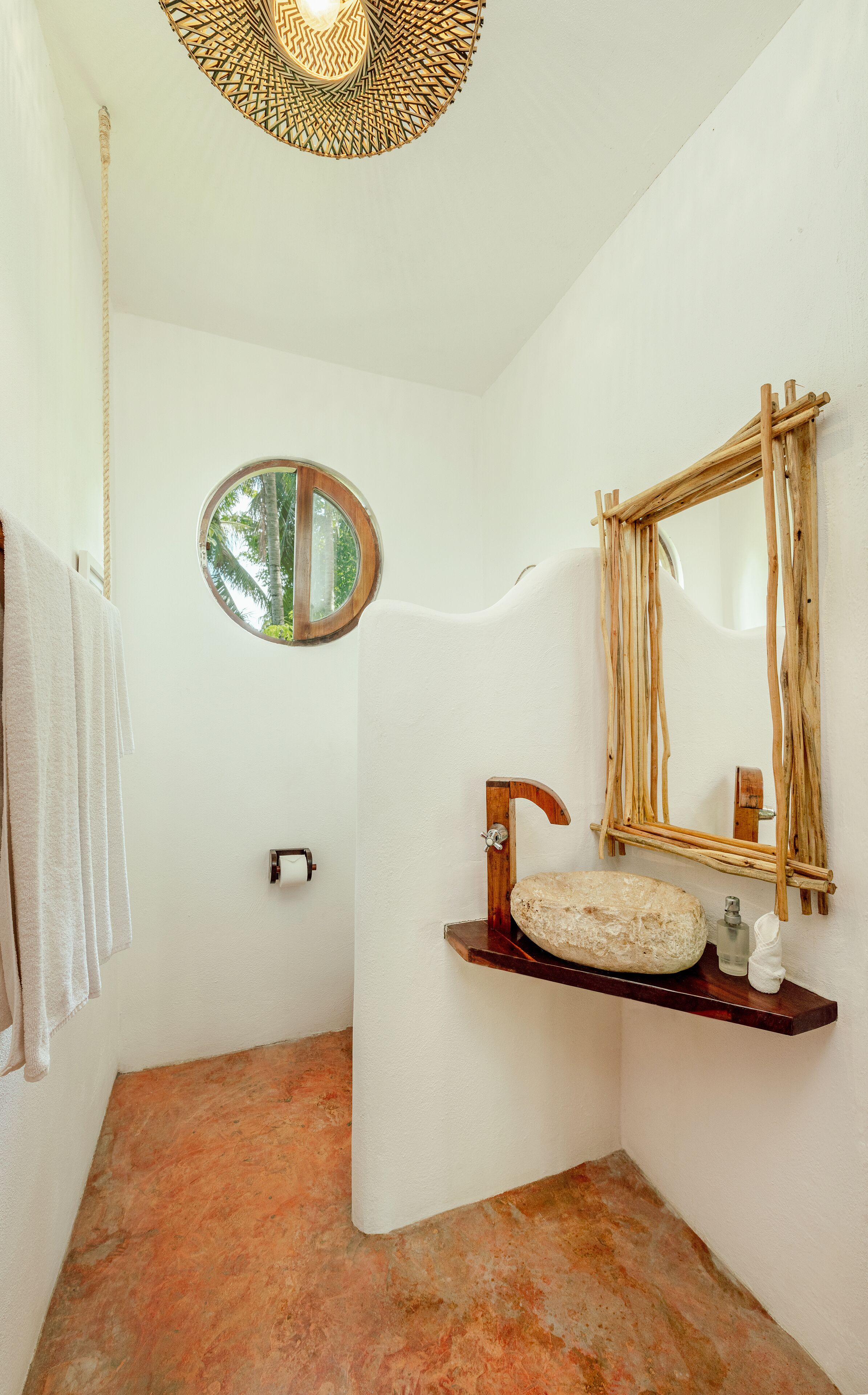 A bathroom with a round mirror, wooden shelf with toiletries, and a towel rack.