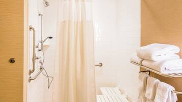 A bathroom with a shower, a toilet, and a towel rack with folded towels.