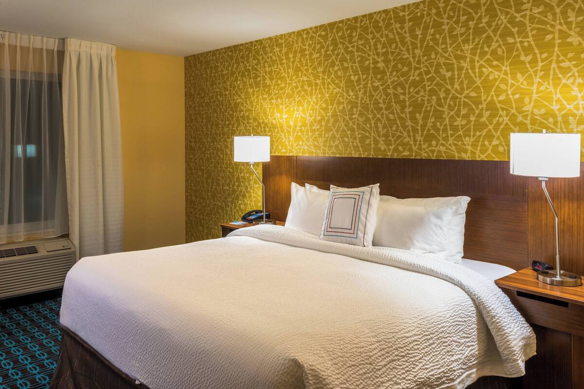 Une chambre d’hôtel avec un grand lit, deux lampes de chevet, une tête de lit en bois et un papier peint à motifs.
