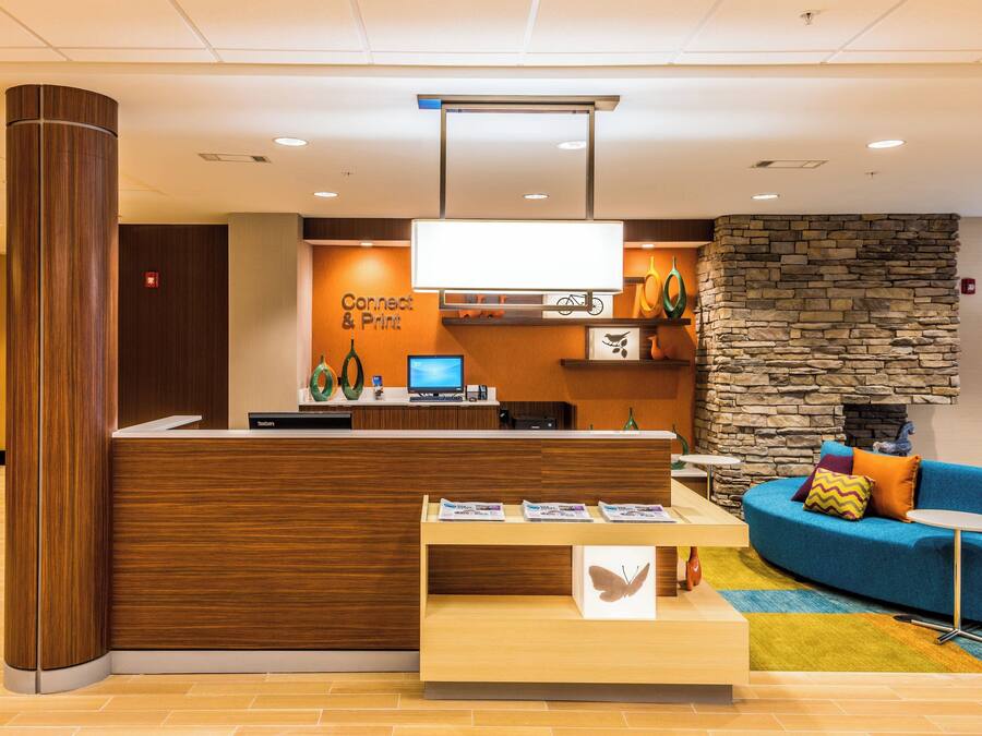 A reception area with a wooden reception desk, a flat-screen TV, a stone wall, and a blue sofa with a small table.