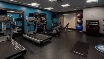 Une salle de sport équipée de tapis de course, de vélos elliptiques et de ballons d’exercice.