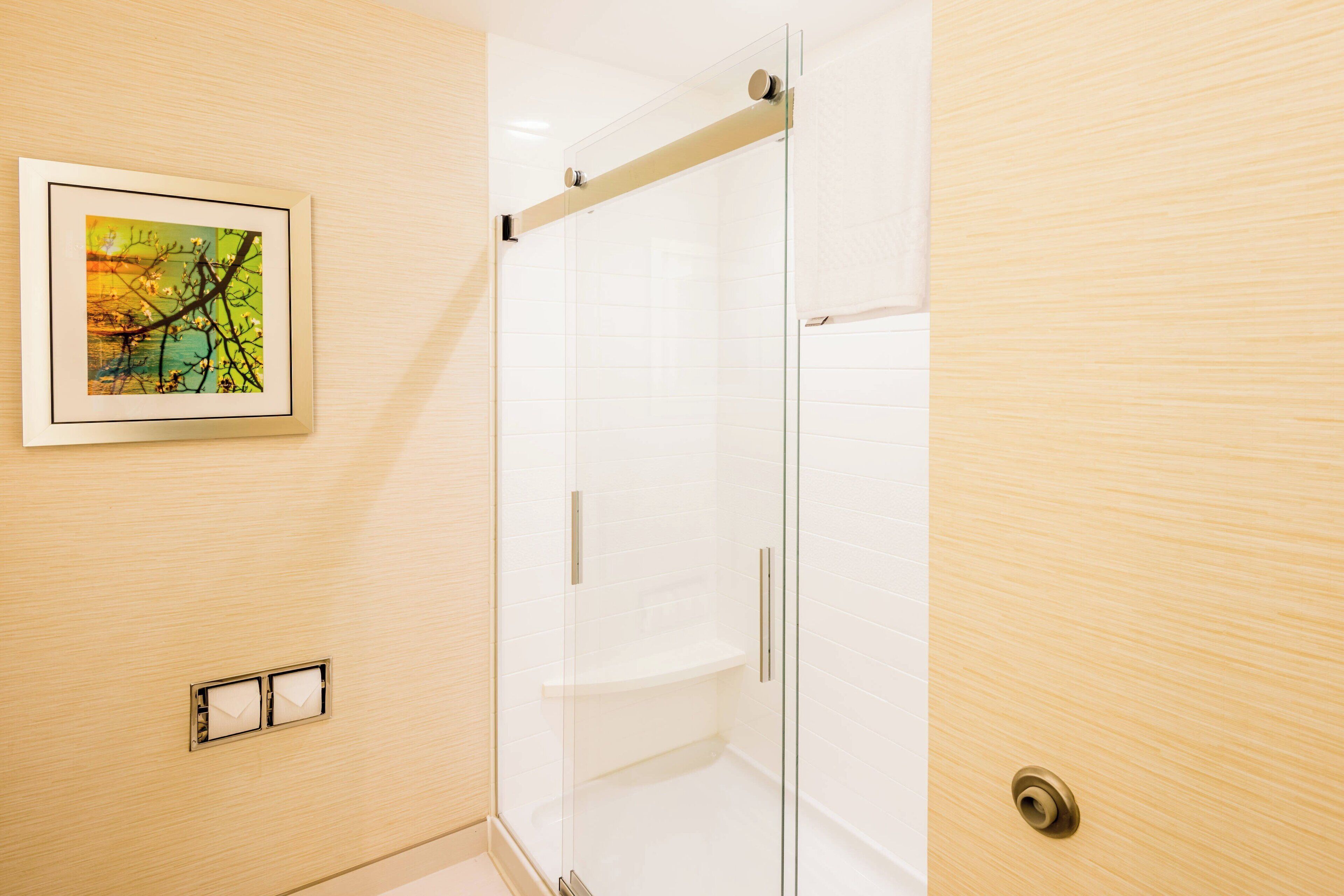 Un baño moderno con cabina de ducha de vidrio, una obra de arte enmarcada en la pared y un perchero para toallas.