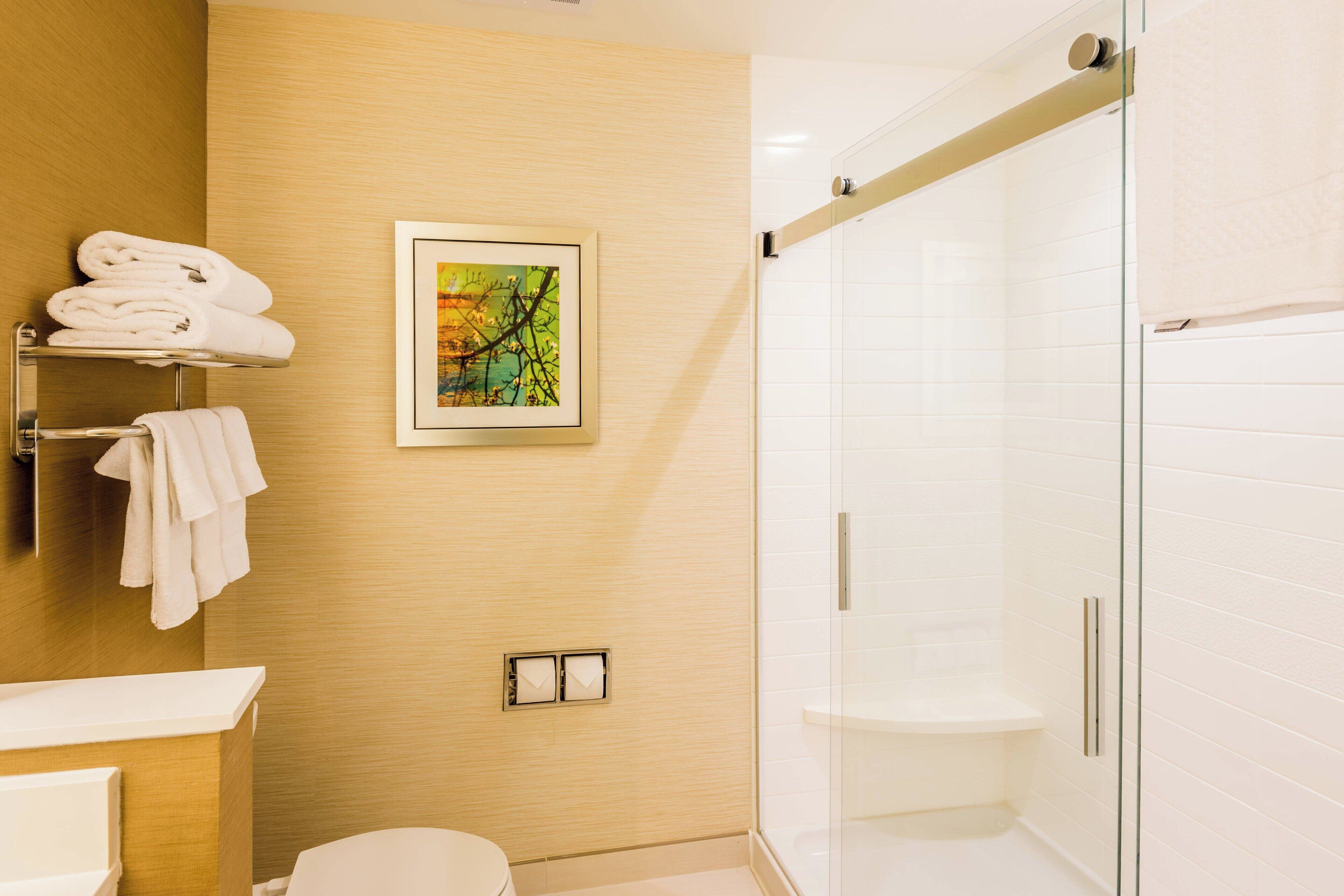 Une salle de bain moderne avec une douche à parois de verre, un meuble-lavabo en bois et une œuvre d’art encadrée au mur.