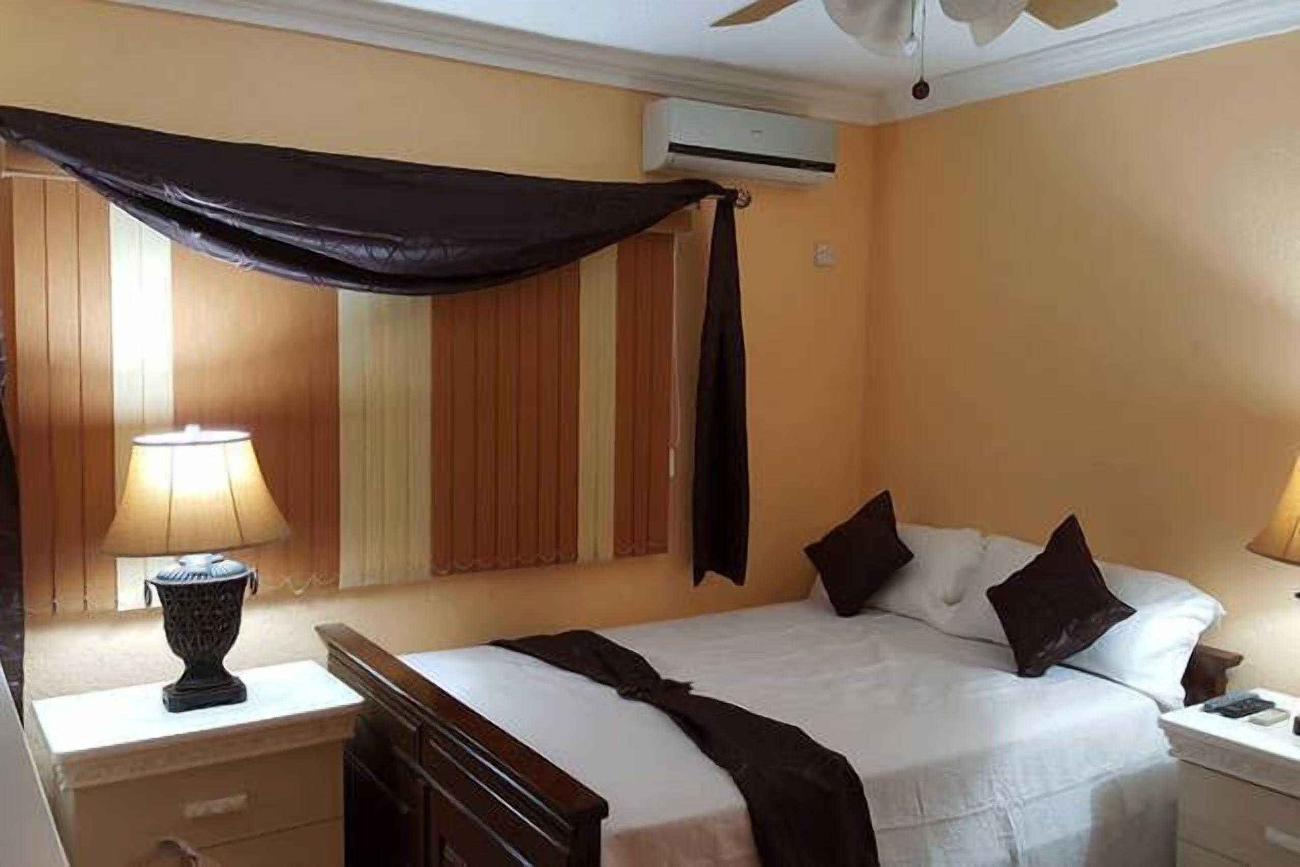 A hotel room with a bed, bedside tables, a lamp, and an air conditioning unit.