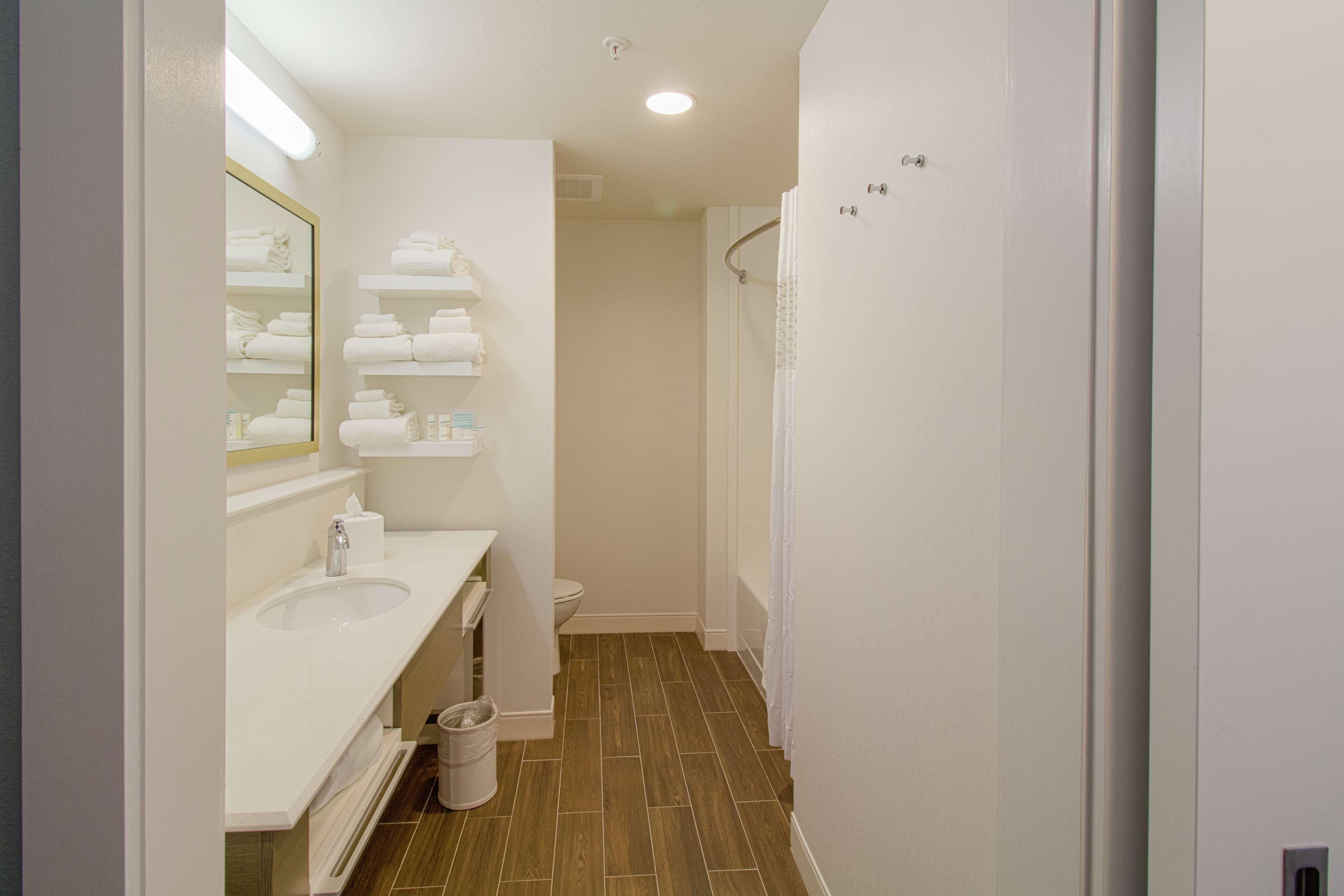 A modern bathroom with a white sink, mirror, and shelves for towels.