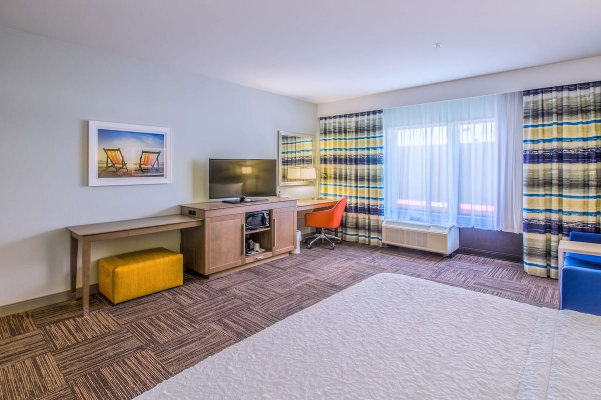 A hotel room with a bed, a desk with a computer, a TV, and a window with curtains.