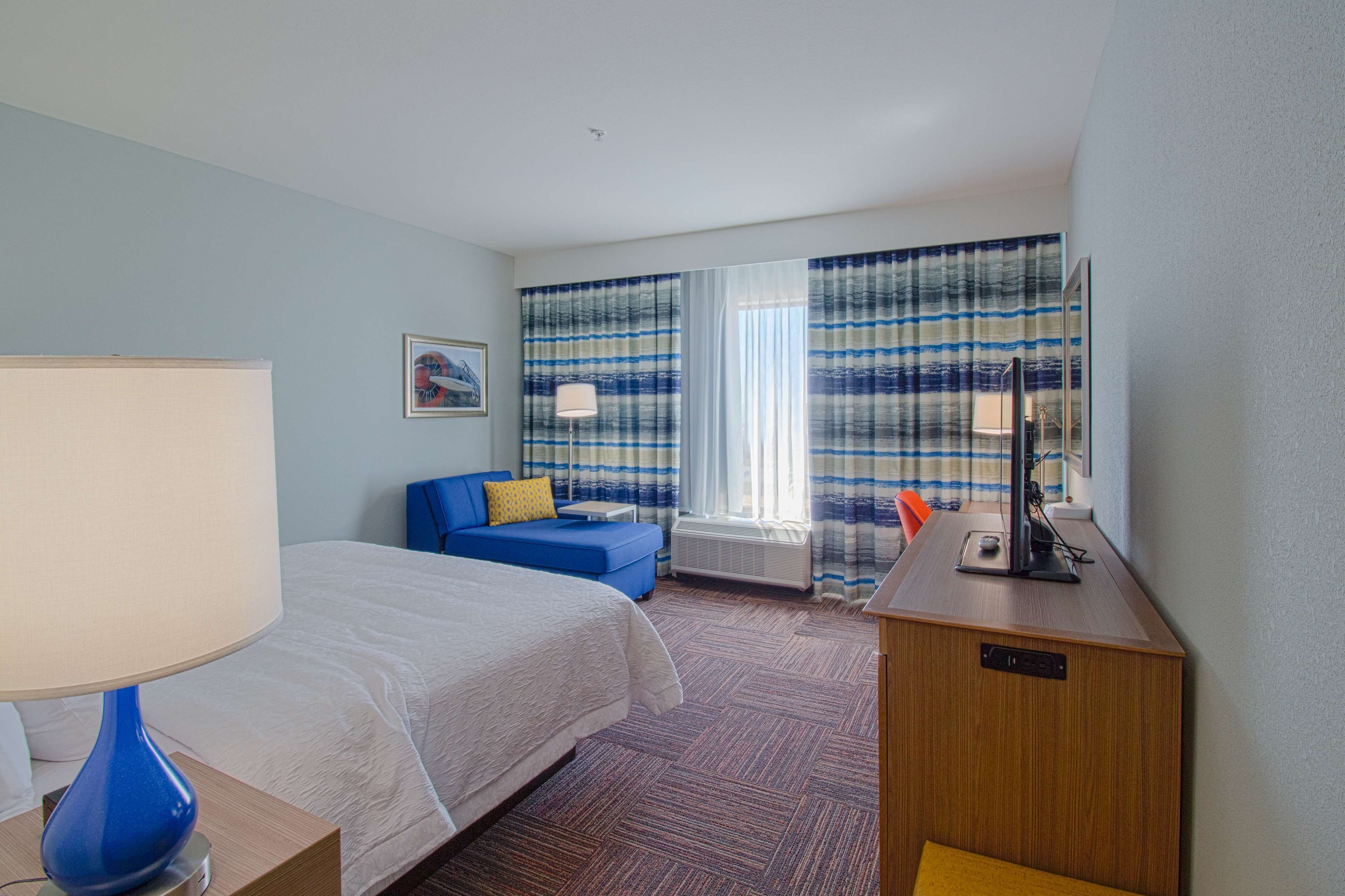 Una habitación de hotel con una cama, un sofá azul, un escritorio con lámpara y una ventana con cortinas.