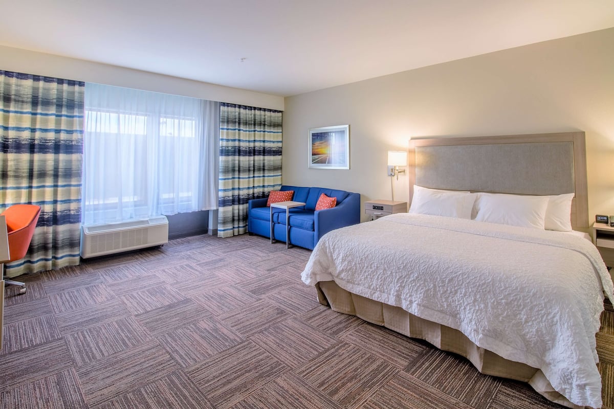 A hotel room with a large bed, a blue sofa, a small table, and a chair.