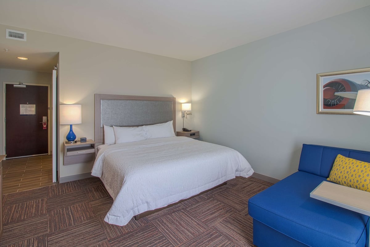A hotel room with a bed, a nightstand, a lamp, a blue sofa, and a painting on the wall.