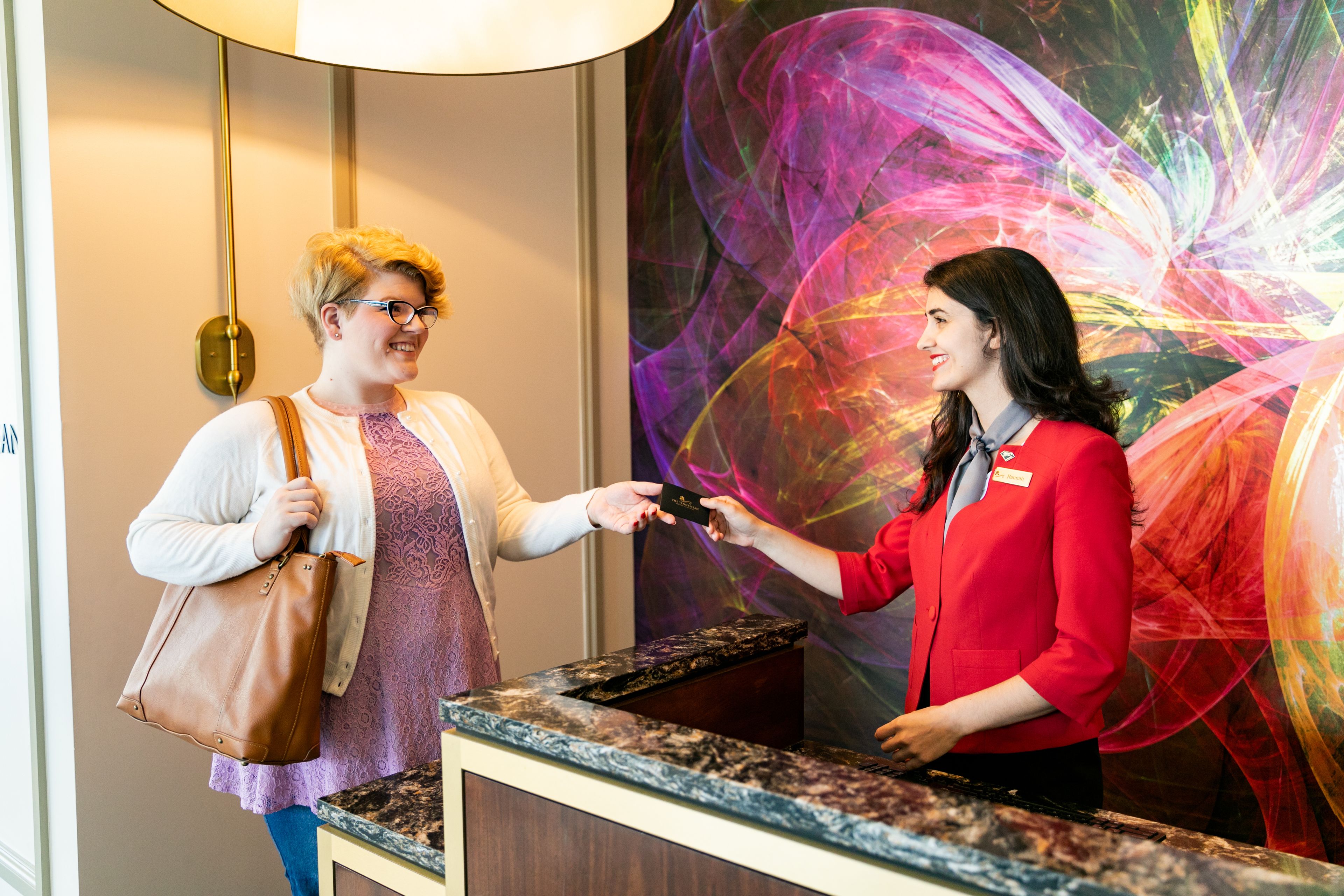 Un espace d’accueil d’hôtel avec un comptoir en marbre, un grand tableau abstrait au mur et un lampadaire doré.
