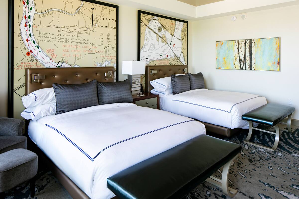A hotel room with two beds, a desk, a chair, and a map on the wall.