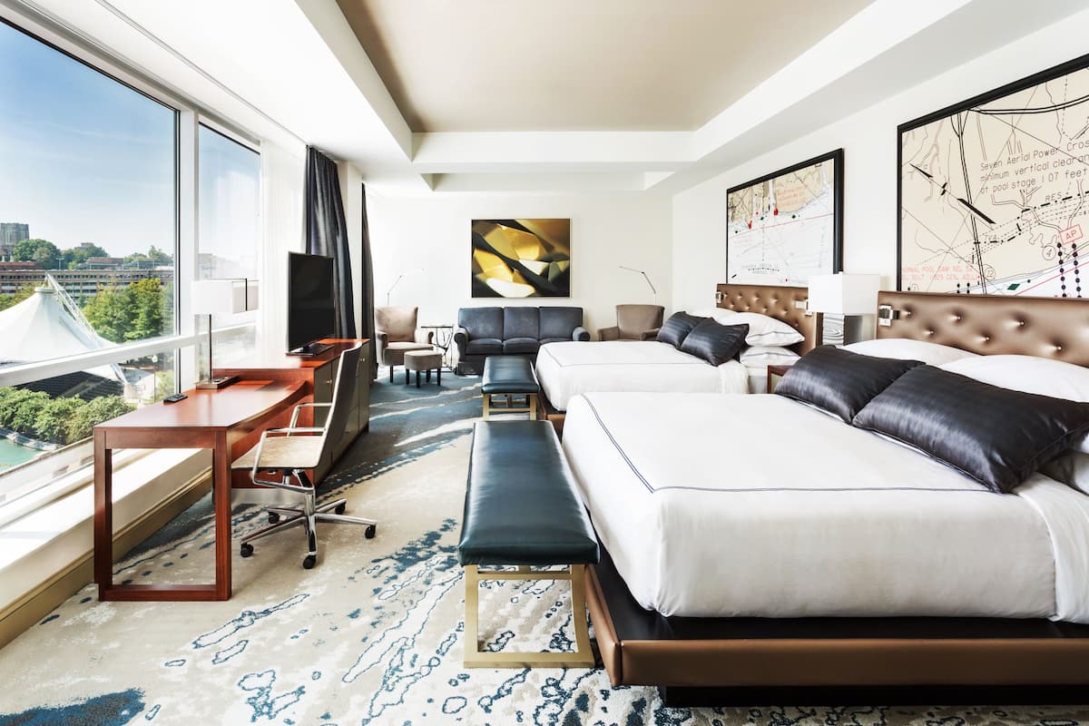 A hotel room with a large window, a desk with a chair, a sofa, a bed, and a map on the wall.