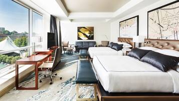 Habitación de hotel con un ventanal grande, un escritorio con silla, un sofá, una cama y un mapa en la pared.