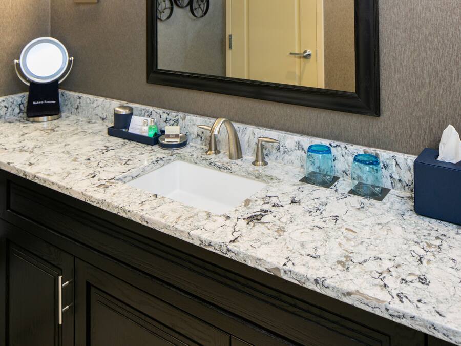 A bathroom with a marble countertop, a sink, a mirror, a wall-mounted light, and a door.