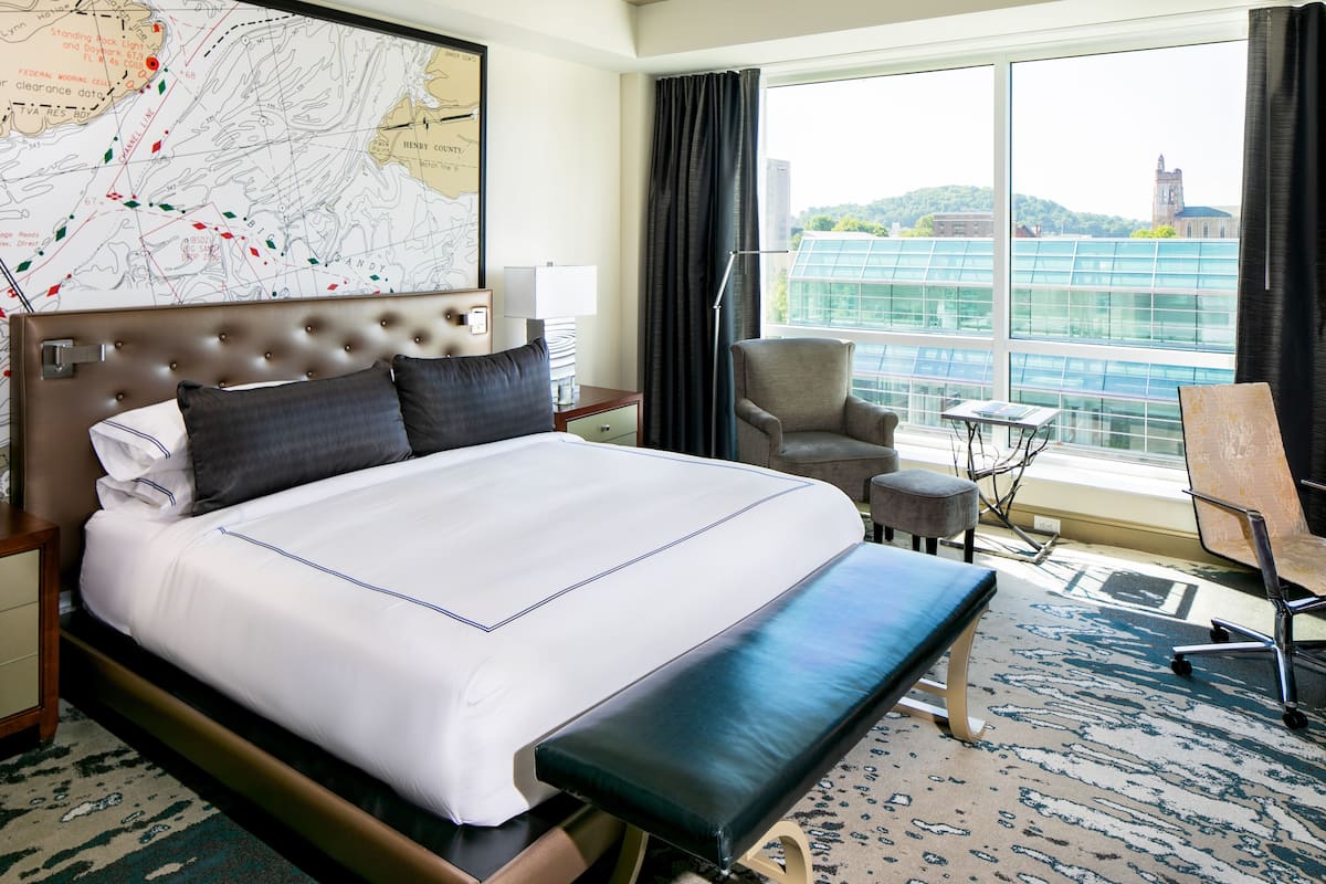 A hotel room with a large bed, a desk, a chair, and a view of a cityscape.